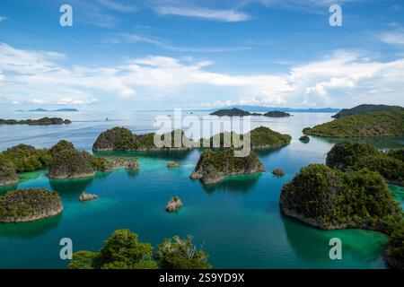 Aerial view of lush green Pianemo Islands in turquoise waters, with boats and distant islands under a clear sky, Fam Islands, Waigeo, Raja Ampat, West Stock Photo