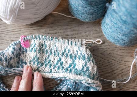 Norwegian knitted pattern in woman hands. Girl holding knitting needles and beautiful knitting pattern. Woman with white and azure knitted pattern. Stock Photo