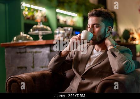 A professional man in a blazer enjoying a cup of coffee in a cozy cafe, highlighting relaxation and sophistication in an elegant setting. Stock Photo
