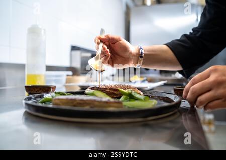 Chef plating grilled fish fillets with soy sauce and fresh vegetables in a professional kitchen, showcasing culinary precision and food artistry. Stock Photo