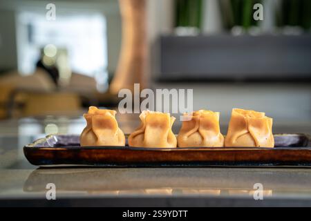 Close-up of four steamed dim sum on a ceramic plate, presented in a modern restaurant ambiance. Focus on gourmet Asian cuisine. Stock Photo