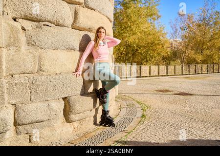 Sporty woman wearing inline skates and sportswear posing near a stone wall in an urban park Stock Photo