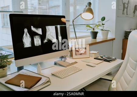 Tidy office workspace with computer displaying X-ray images. Desk includes keyboard, mouse, plants, and personal items creating a productive environment Stock Photo