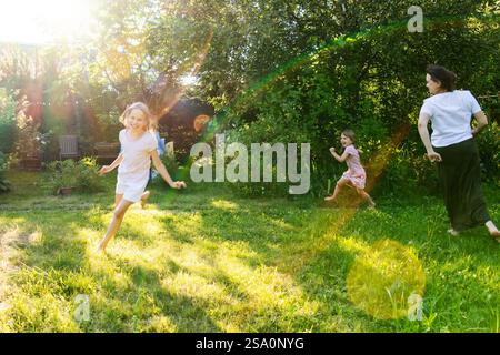 A joyful family moment as a mother and her two daughters run together in a lush green backyard on a sunny summer day, laughing and playing amidst natu Stock Photo