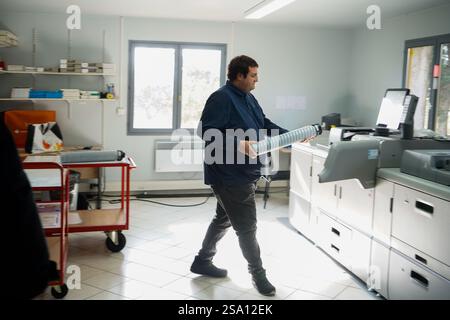 Disabled worker working in the printing, reprography and marking workshop. Replacing an ink cartridge on the printer. Stock Photo