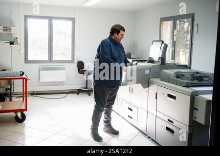 Disabled worker working in the printing, reprography and marking workshop. Replacing an ink cartridge on the printer. Stock Photo