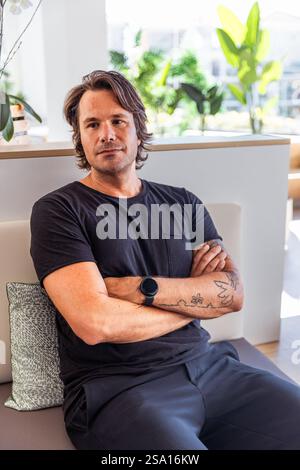 A man with a watch on his wrist sits on a couch with his arms crossed, photo with copy space. Concept of relaxation and comfort Stock Photo