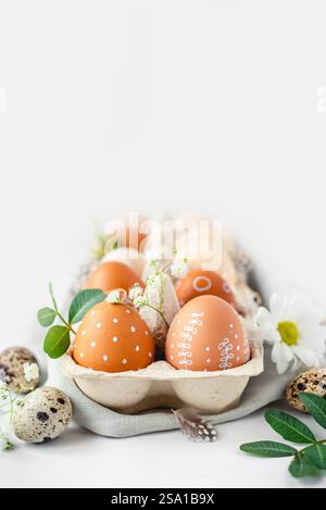 A delicate Easter background with hand-painted eggs in a box on a white table. Easter composition with flowers and feathers Stock Photo