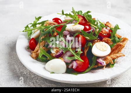 A warm salad with fried chicken fillet, arugula and cherry tomatoes, and boiled quail eggs, on a white plate, no people Stock Photo