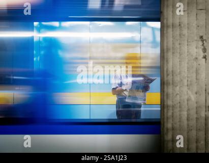 A blurred image of a subway station with a person reading a newspaper. The background shows a moving train, creating a sense of motion. The colors are Stock Photo