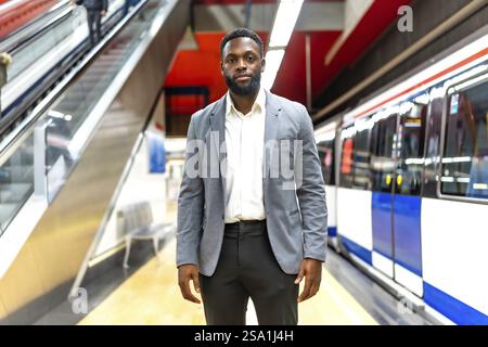 Young businessman standing on a subway platform, waiting for his train, symbolizing urban commuting and modern transportation Stock Photo