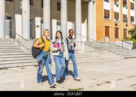 Horizontal full length photo with copy space of three university students with notebooks and rucksack walking along the campus Stock Photo