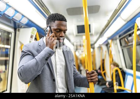 Young businessman having phone call while commuting on subway train, holding onto handrail Stock Photo