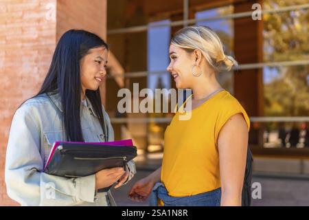 Two multi-ethnic female cauacsian and chinese students discussing outside the university entrance Stock Photo