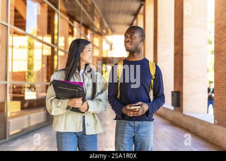 Two african and chinese multi-ethnic exchange students arriving at the university walking and talking together Stock Photo