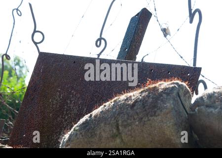 A rusted metal plate, likely part of a barrier or fortification, is affixed to a stone wall.  The presence of barbed wire suggests a historical contex Stock Photo