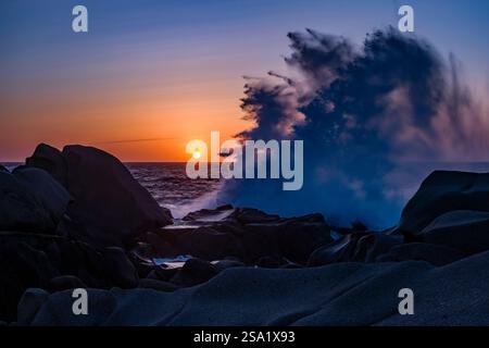 Big wave breaking on one of the bizarre granite rock formations on Capo Testa, the northernmost point of the Peninsula, at sunset. Stock Photo