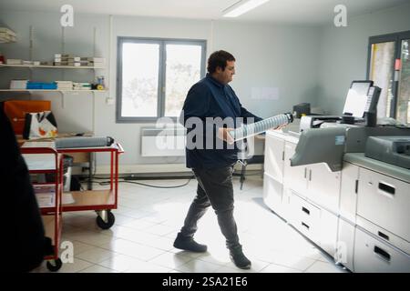 Disabled worker working in the printing, reprography and marking workshop. Replacing an ink cartridge on the printer. work with disabilities 016794 026 Stock Photo