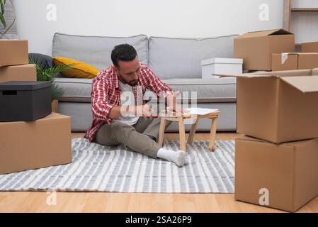 young man assembles DIY shelf moving carton boxes, resourcefulness in his new home after relocating Stock Photo