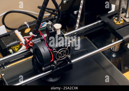 This is a detailed closeup view of a 3D printer equipped with a cooling fan on top of it, showcasing its intricate design and components Stock Photo