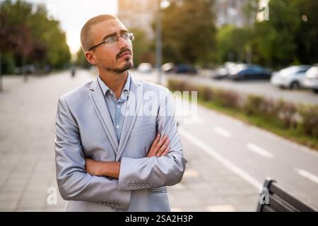 Portrait of thoughtful and distraught young businessman who is standing in the street and looking away. Stock Photo