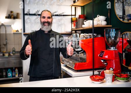 Professional barista in black apron working in restaurant. Portrait of happy barmen who is making coffee in his bar. Stock Photo