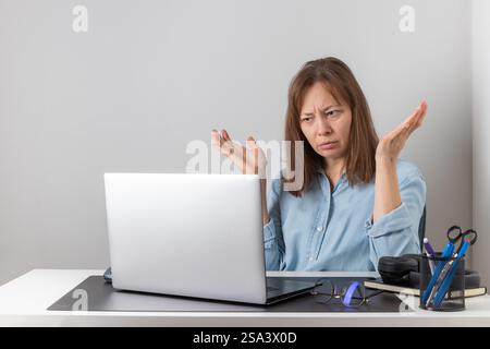 What is wrong. Anxious frustrated female office worker sitting at desk with pc laptop and getting angry. Irritated freelancer woman looking at laptop Stock Photo