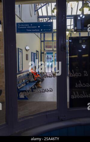 Man in a high viz jacket sitting at Kings Lynn Station - viewed through the cafe window Stock Photo
