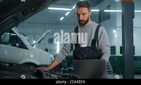 Caucasian man mechanic working in car service workshop fixing engine using laptop electronic diagnostics test repair vehicle automobile with computer Stock Photo