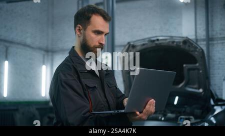 Professional mechanic Caucasian man in uniform male industrial worker technical mechanical engineer using laptop check automobile diagnostics auto Stock Photo