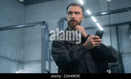 Mechanic man auto mechanical worker using mobile phone gadget in repair car service garage automobile factory pensive thoughtful male guy repairman Stock Photo