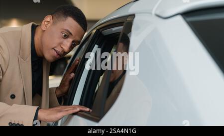 African American ethnic man smiling customer client looking inside car salon in dealership store male owner businessman buyer touching automobile Stock Photo