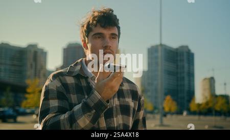 Caucasian handsome man hold mobile phone recording voice message in city happy cheerful smiling male guy businessman walking sending audio voicemail Stock Photo