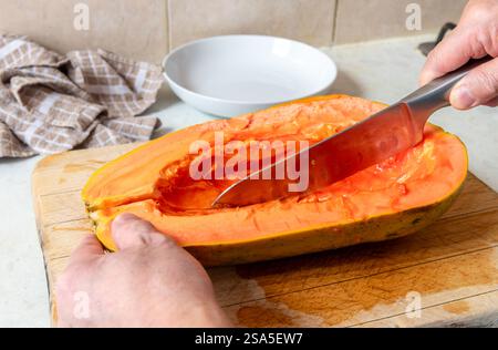 A person slicing a half papaya with the seeds cleaned out. Stock Photo