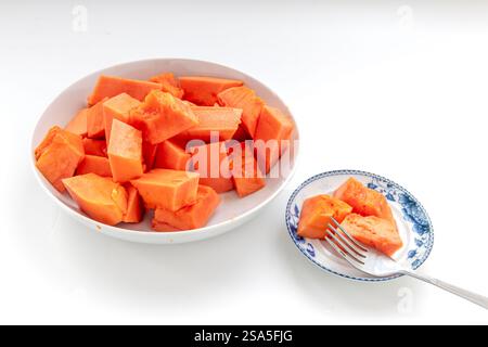 Sweet soft cut pieces of ripe papaya served on plates with a fork isolated on white. Stock Photo