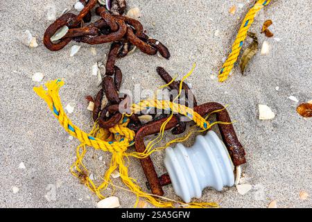 Metal chains with a rusty pulley, yellow rope with blue highlights broken on beach sand, parts of fishing boat, environmental pollution concept, winte Stock Photo