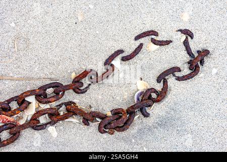Beach shore with rusty metal chain lying on sand, remains of broken shells, parts of a fishing boat, environmental pollution concept, winter day Stock Photo