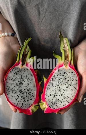 A close-up of female hands holding two halves of a sliced pitahaya, also known as dragon fruit. Vertical crop. Close up. Stock Photo