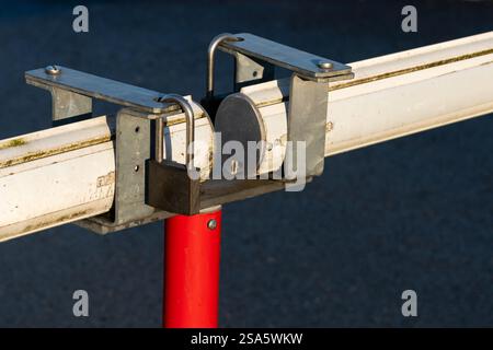 A sturdy lock firmly secures a horizontal rail mounted on a bright red pole in a clear outdoor environment. The setup appears practical for safety or organization purposes. Stock Photo