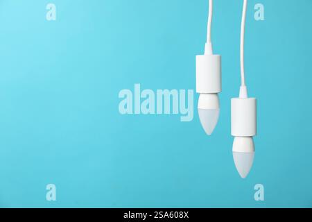 Light bulbs hanging on cords against blue background, space for text Stock Photo