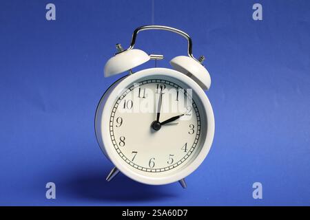 White alarm clock in air on blue background Stock Photo