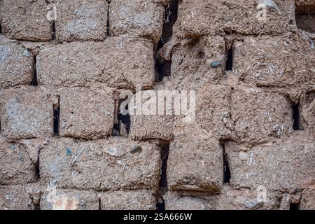A brick wall with a lot of holes in it. The wall is made of mud and has a lot of dirt on it Stock Photo