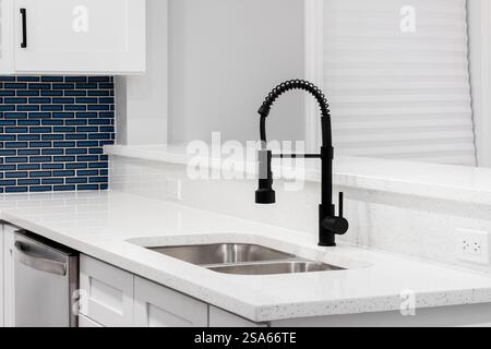 A kitchen detail with a black faucet, white quartz countertops, and a blue glass subway tile backsplash. Stock Photo