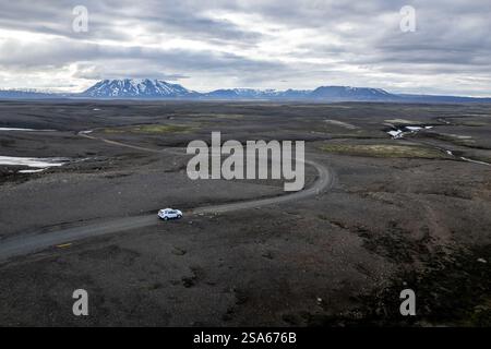 Aerial drone view remote landscape road with mountains and white car 4x4 under cloudy weather in Iceland Stock Photo