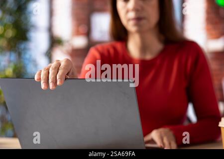 Casual woman opening her laptop at home office to solve daily tasks, doing remote freelance work online. Person surfing the web multitasking in her loft apartment, tech savvy. Stock Photo