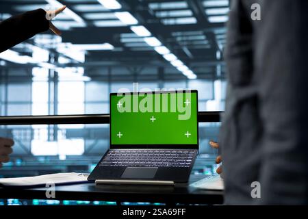 System administrators in data center using green screen mockup notebook, observing analytics, reviewing equipment health. Server room employees using chroma key laptop, adjusting system parameters Stock Photo