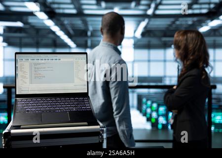 Focus on lines of code on laptop display used by teamworking data center colleagues to run security patches. Close up of programming language on notebook used by server room IT experts scanning gear Stock Photo