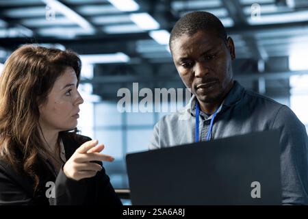Teamworking coworkers in data center workspace using automation tools on tablet. IT staff members ensuring continuous uptime of server farm, managing data flows with device Stock Photo
