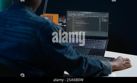 Software developer writes code on laptop screen while in apartment office using Java programming languages. Programmer remotely working on fixing database errors while working from home, camera A Stock Photo