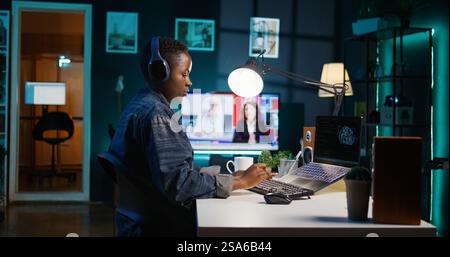Computer scientist updating artificial intelligence neural networks, writing binary code scripts. Remote worker in apartment office uses digital device programming to upgrade AI, camera B Stock Photo